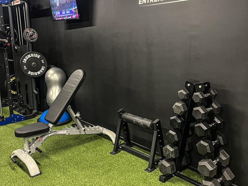 Zona de entrenamiento con muro corporativo, banco y mancuernas